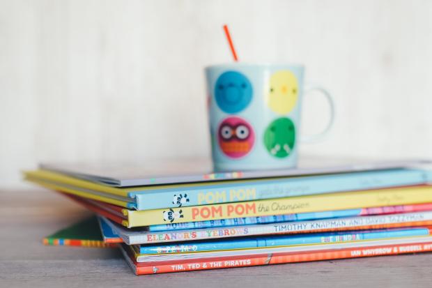 Halesowen News: Children's books in a pile with a colourful mug on top. Credit: Canva